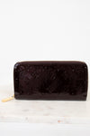 Maroon patent leather wallet with brand logo on a white marble surface