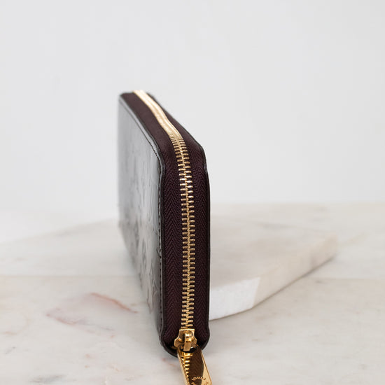 Side of maroon wallet with gold zipper on a marble surface