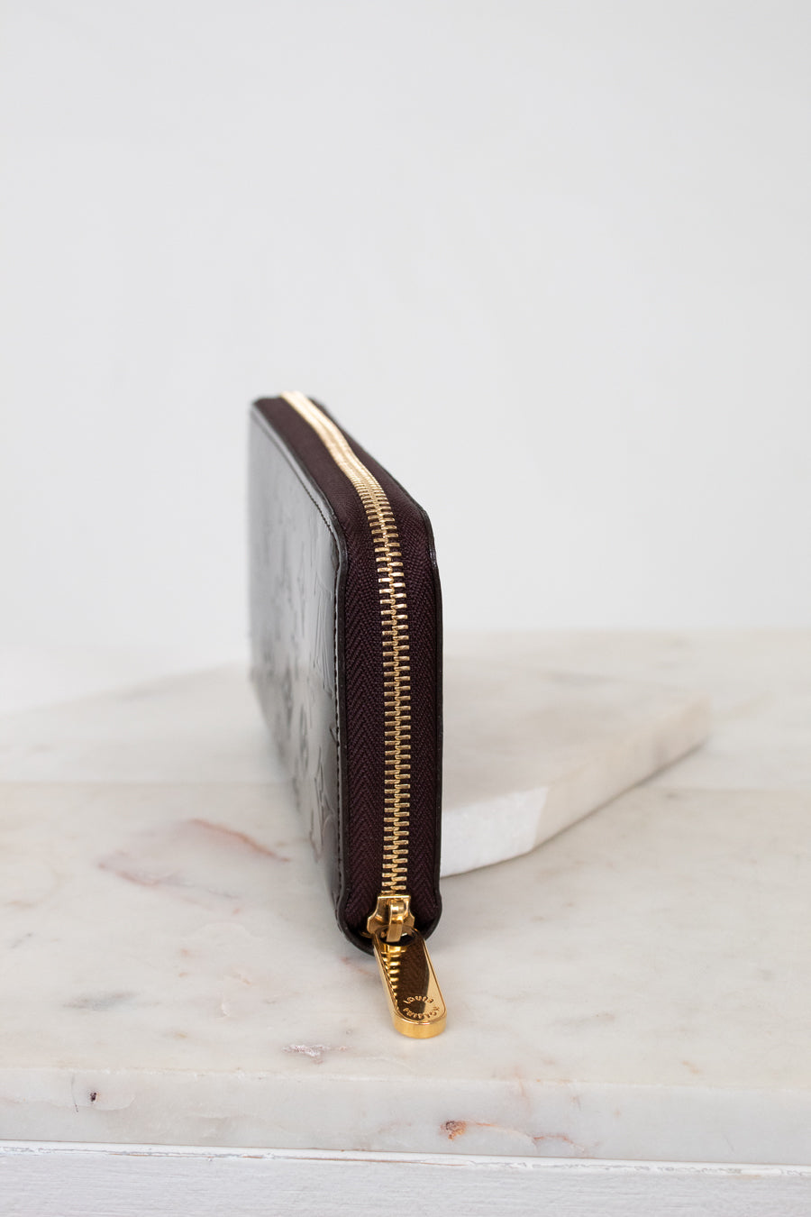 Side of maroon wallet with gold zipper on a marble surface