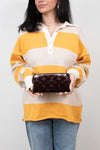 Person wearing a striped sweater holding a maroon patent leather wallet against a plain background