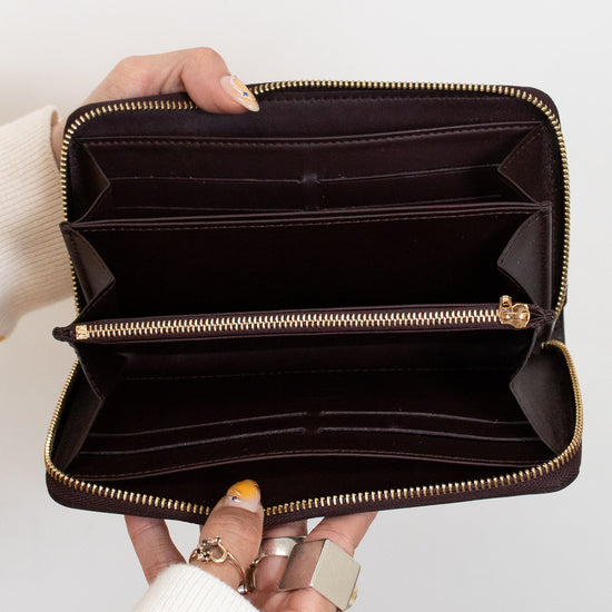 Hand holding an open brown interior of wallet with gold zipper on a white background
