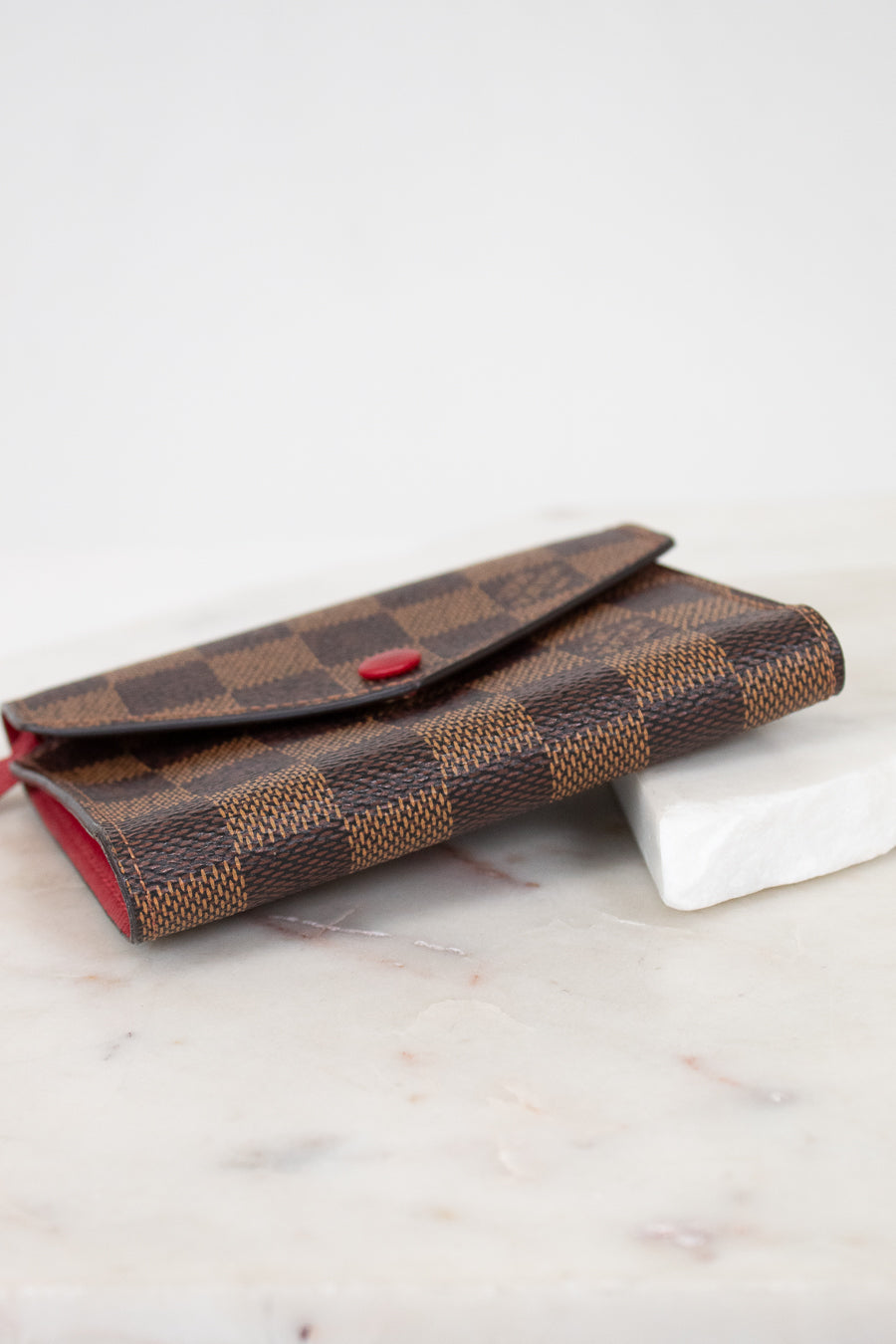 Brown checkered wallet with red accents on a marble surface
