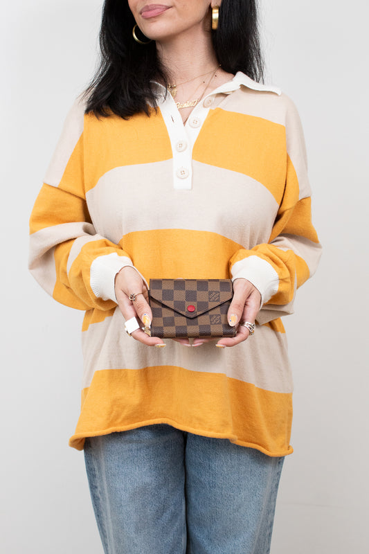 Person wearing a striped shirt holding a small wallet against a plain background