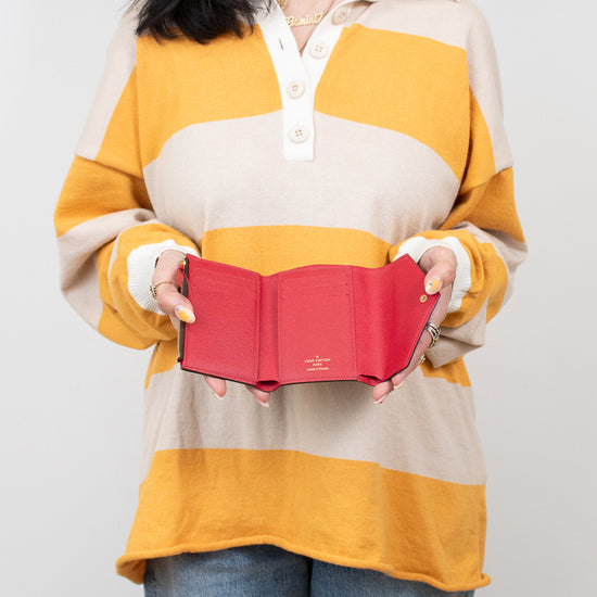 Person wearing a yellow and beige striped shirt holding an open red wallet against a white background