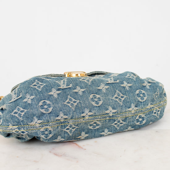 A Louis Vuitton monogrammed denim bag viewed from the bottom with a gold-tone clasp, resting on a light marble surface against a white background.