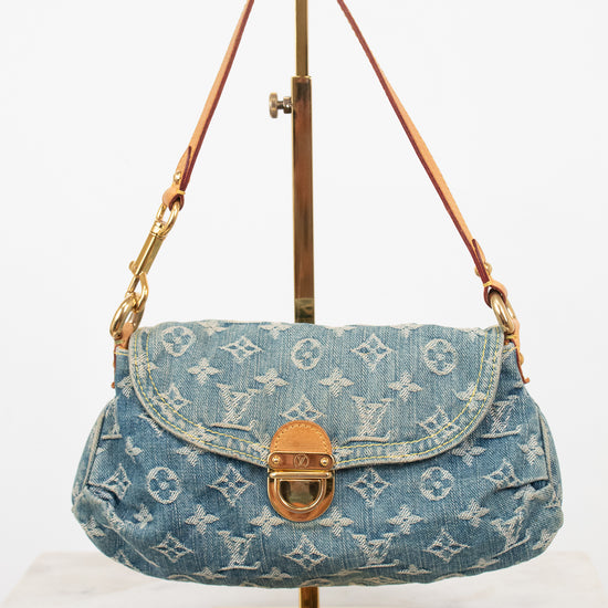 A Louis Vuitton monogram denim shoulder bag in blue, displayed on a gold metal stand against a white background.