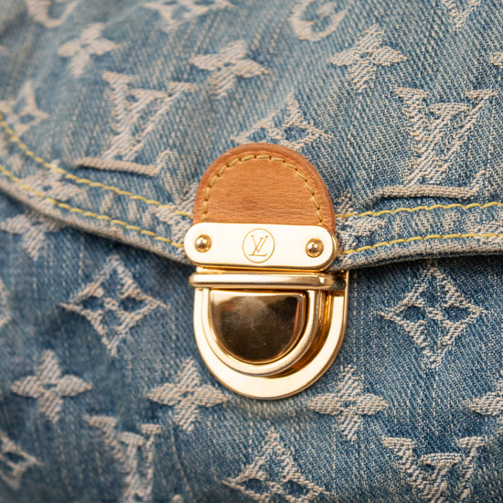 Close-up of a Louis Vuitton monogram canvas handbag in blue denim, featuring a gold-tone D-ring clasp with a brown leather accent.