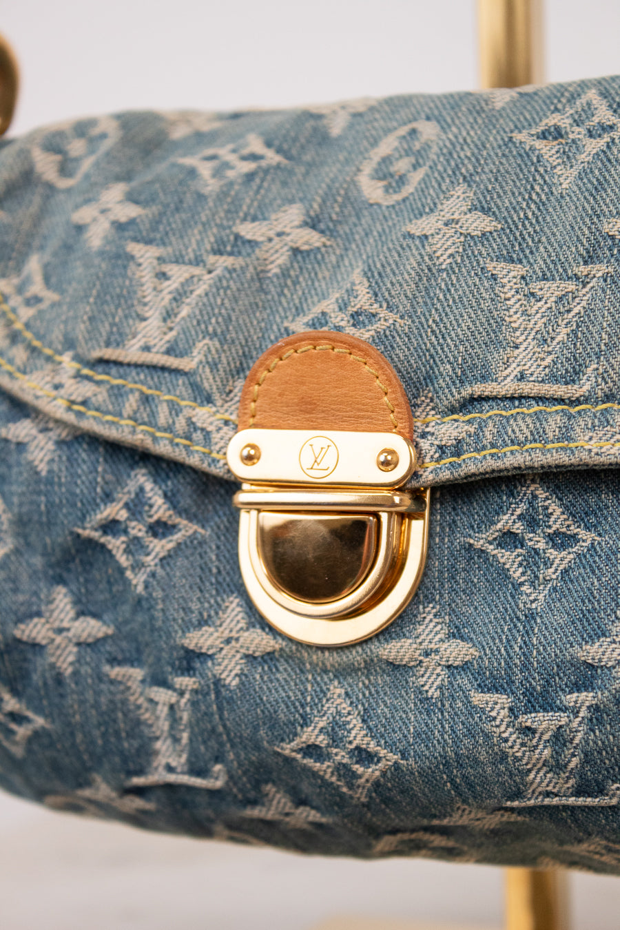 Close-up of a Louis Vuitton monogram canvas handbag in blue denim, featuring a gold-tone D-ring clasp with a brown leather accent.