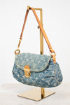 A Louis Vuitton monogram canvas shoulder bag in light blue denim, displayed on a gold metal stand against a white background.