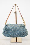A Louis Vuitton denim shoulder bag with the brand's signature monogram pattern, displayed on a gold-colored stand against a white background.