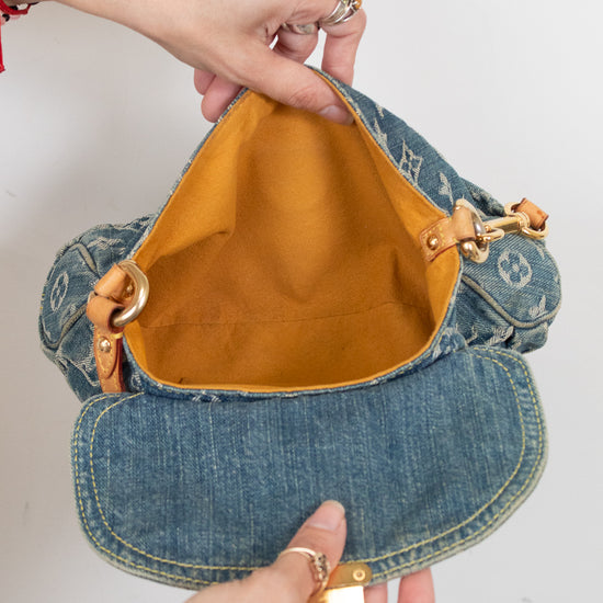 A denim shoulder bag with a mustard yellow interior lining, held open by two hands against a plain white background.