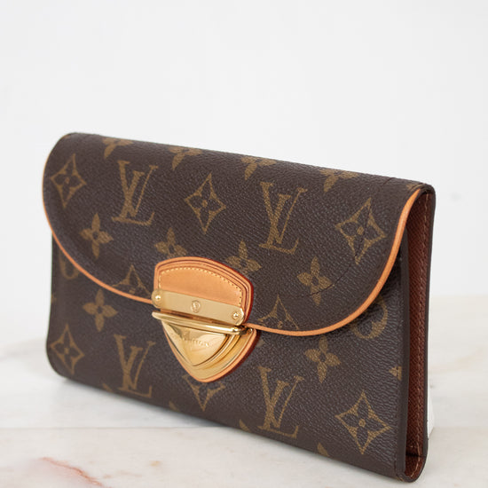 A Louis Vuitton monogram coated canvas clutch wallet with a brown coated canvas flap and gold-tone metal clasp, resting on a light marble surface against a white background.