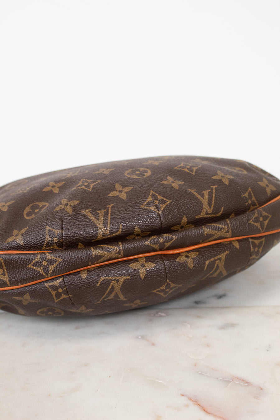 A Louis Vuitton monogram canvas pouch or small bag resting on a light marble surface against a white background.