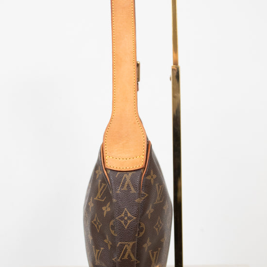 A Louis Vuitton monogram shoulder bag in brown coated canvas with tan leather trim, displayed on a gold metal stand against a white background.