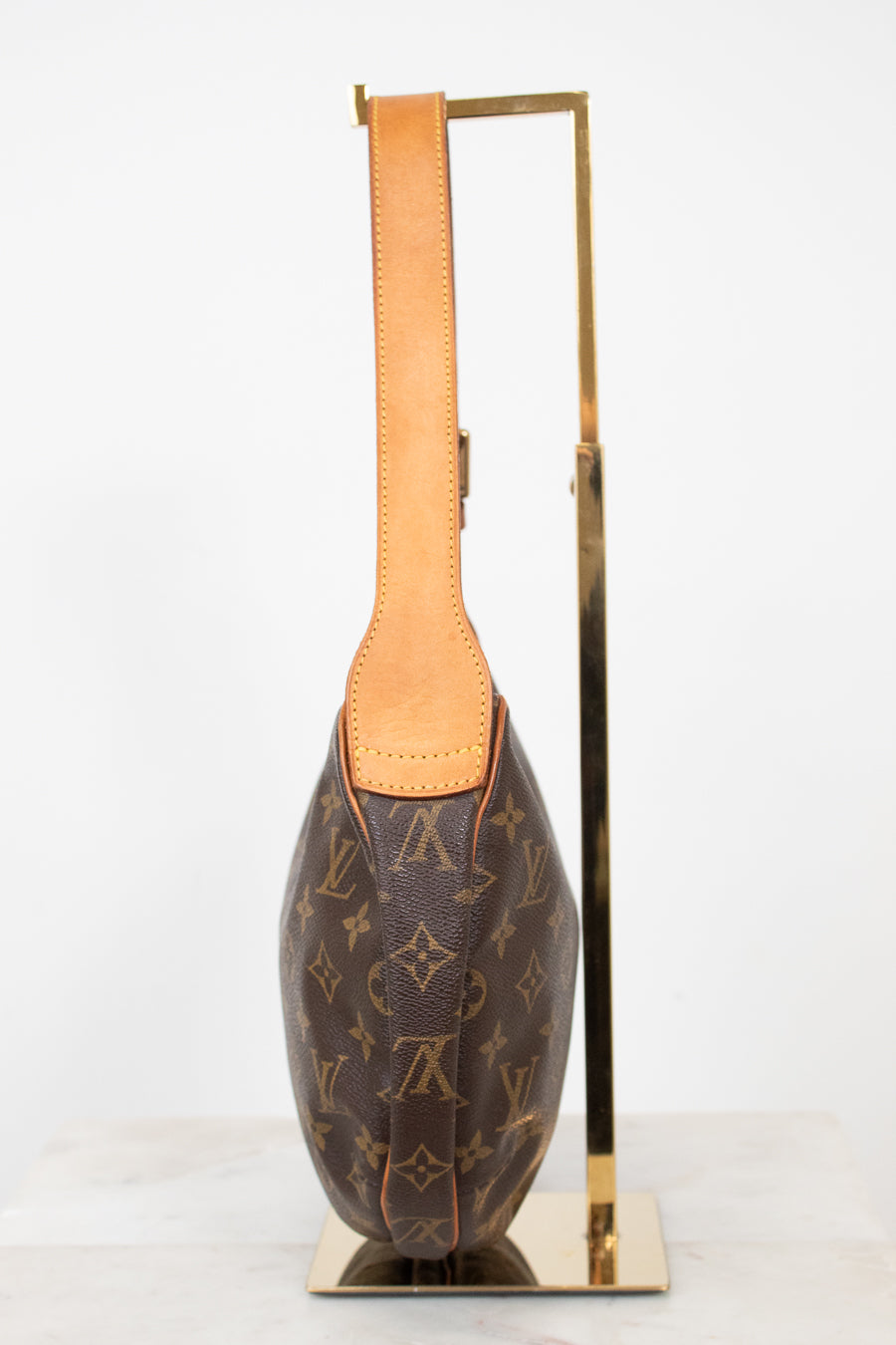 A Louis Vuitton monogram shoulder bag in brown coated canvas with tan leather trim, displayed on a gold metal stand against a white background.