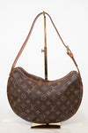 A Louis Vuitton monogram canvas crescent shoulder bag displayed on a gold-colored metal stand against a white background.