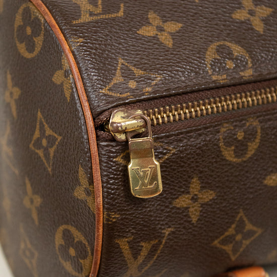 Close-up of a Louis Vuitton monogram canvas cylindrical bag with brown leather trim and gold-tone hardware on a light marble surface.