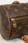 Close-up of a Louis Vuitton monogram canvas cylindrical bag with brown leather trim and gold-tone hardware on a light marble surface.