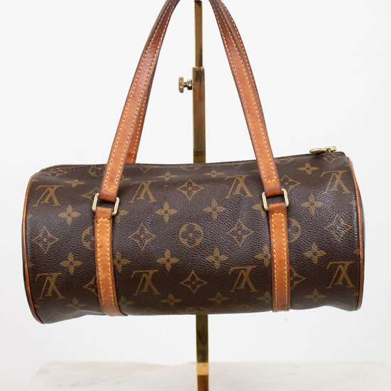 A Louis Vuitton monogram canvas duffle bag with tan leather handles and trim, displayed on a gold metal stand against a white background.