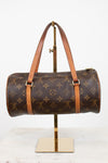 A Louis Vuitton monogram canvas duffle bag with tan leather handles and trim, displayed on a gold metal stand against a white background.