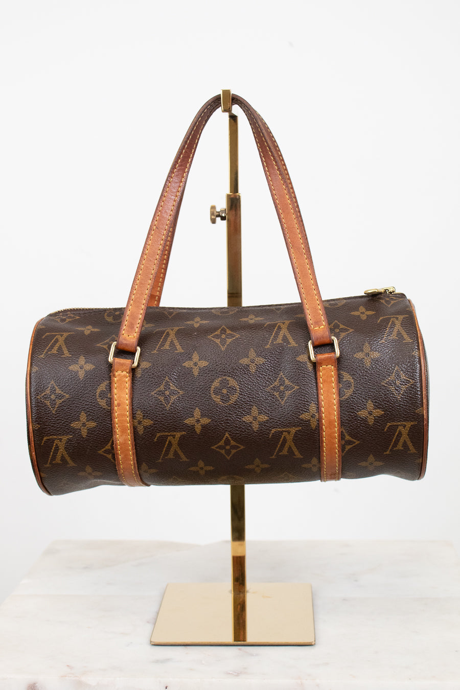A Louis Vuitton monogram canvas duffle bag with tan leather handles and trim, displayed on a gold metal stand against a white background.