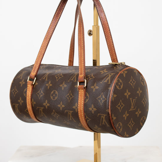 A Louis Vuitton monogram canvas duffle bag with brown leather handles, displayed on a gold-colored stand against a white background.