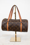 Louis Vuitton monogram canvas duffle bag with tan leather handles and trim, displayed on a gold stand against a white background.