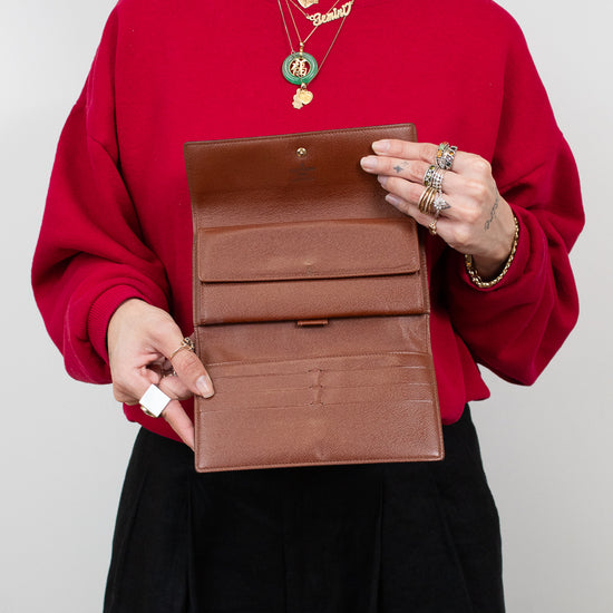 Person wearing a red sweater holding open a brown leather wallet against a plain background