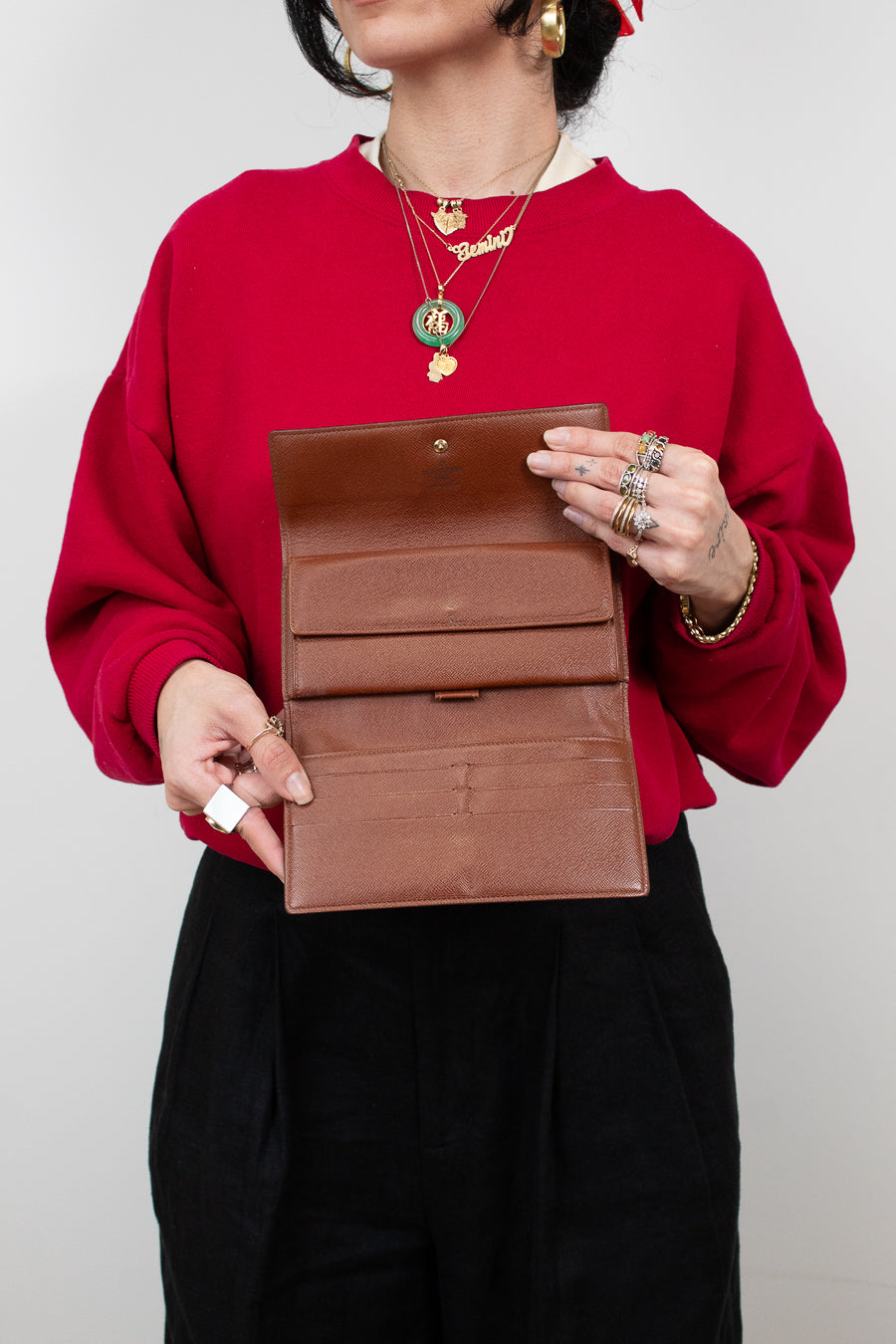Person wearing a red sweater holding open a brown leather wallet against a plain background