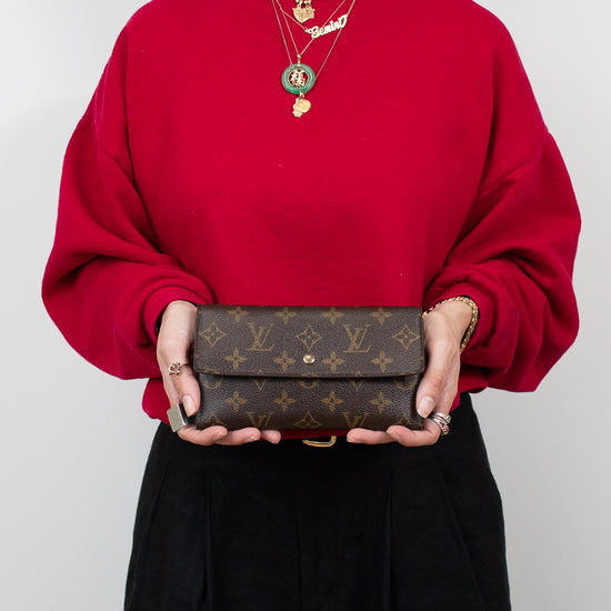 Person wearing a red sweater holding a brown wallet with a visible brand logo.