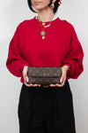 Person wearing a red sweater holding a brown wallet with a visible brand logo.