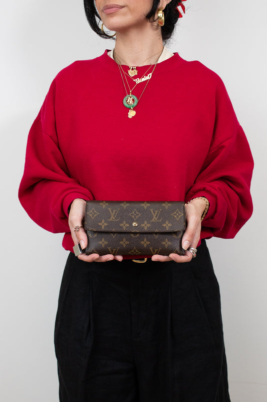 Person wearing a red sweater holding a brown wallet with a visible brand logo.