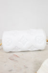 A white cylindrical shoulder bag with embossed Louis Vuitton-style monogram motifs, resting on a light marble surface against a white background.
