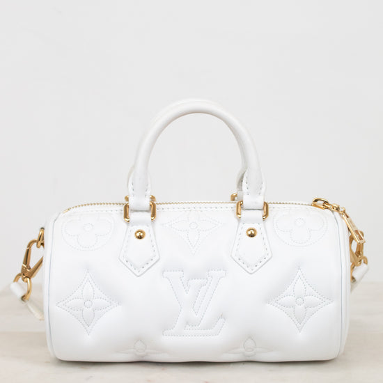 A white leather Louis Vuitton handbag with embossed monogram pattern and gold-tone hardware, shown on a light marble surface against a white background.