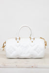 A white leather Louis Vuitton handbag with embossed monogram pattern and gold-tone hardware, shown on a light marble surface against a white background.