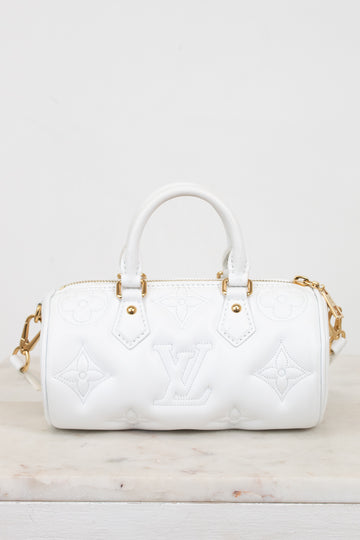 A white leather Louis Vuitton handbag with embossed monogram pattern and gold-tone hardware, shown on a light marble surface against a white background.