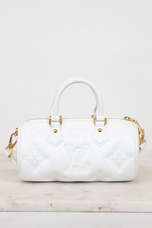 A white leather Louis Vuitton handbag with embossed monogram pattern and gold-tone hardware, shown on a light marble surface against a white background.