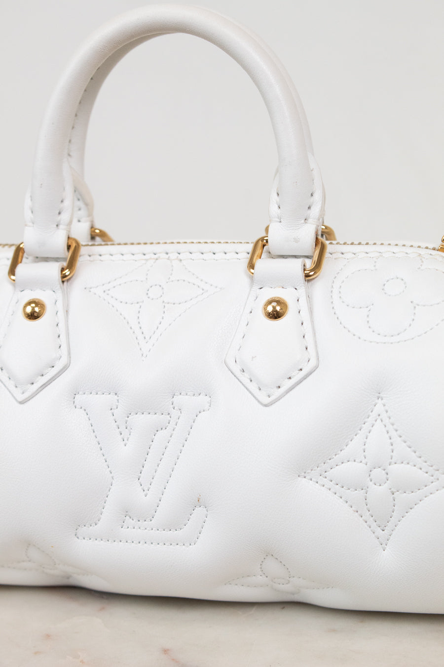 White leather handbag with embossed Louis Vuitton monogram pattern and gold-tone hardware, shown in a close-up studio-style shot.