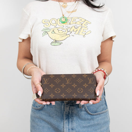 Person wearing a white t-shirt with a cartoon character design, holding a Louis Vuitton wallet.