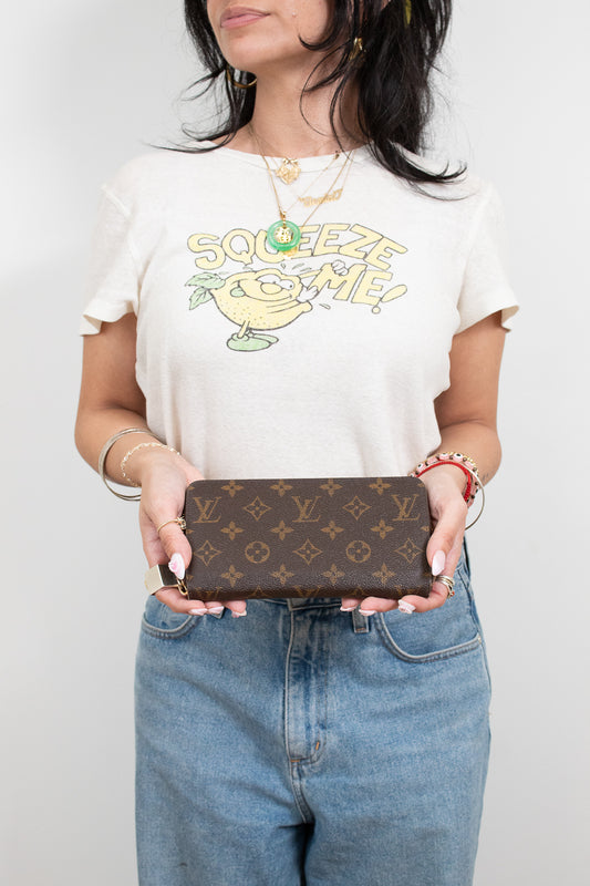 Person wearing a white t-shirt with a cartoon character design, holding a Louis Vuitton wallet.