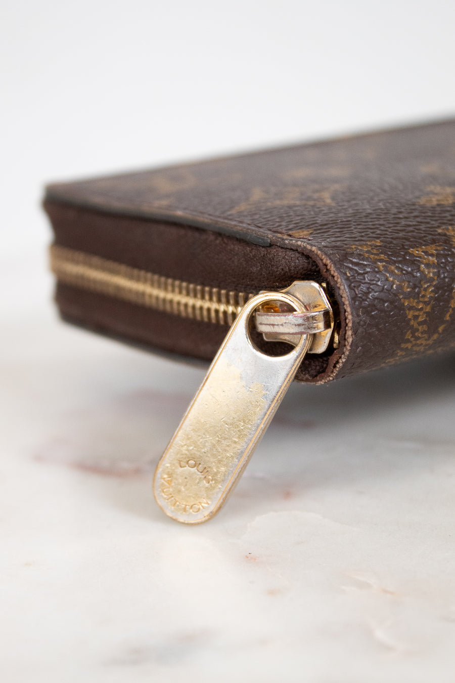 Close-up of a brown wallet with gold zipper pull on a light background