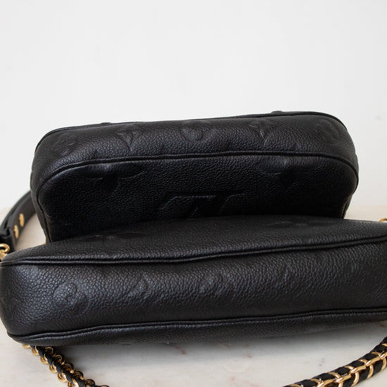 Underside of a black leather shoulder bag with gold-tone hardware and a chain strap, against a light gray background.