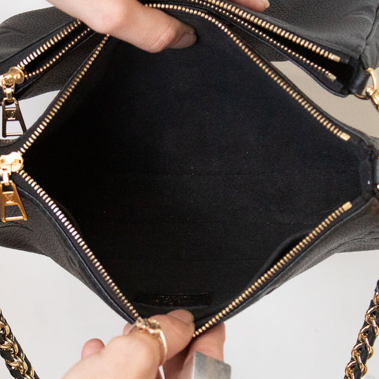 Hands holding open a purse showing a black interior of a black leather shoulder bag with gold-tone hardware and a chain strap, against a light gray background.