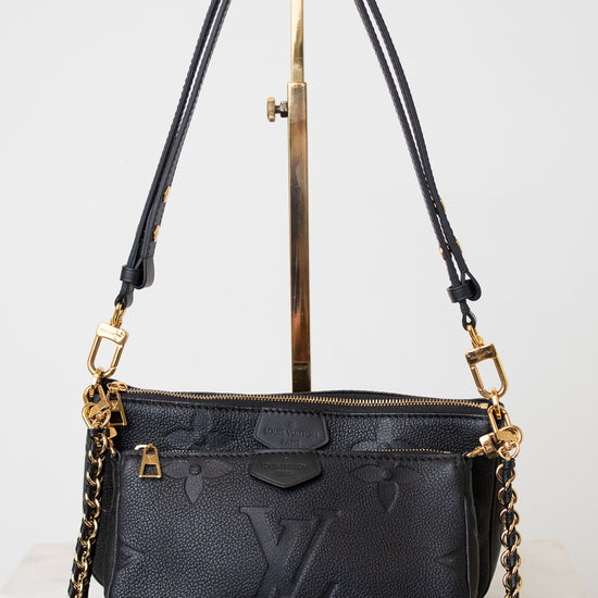 A black Louis Vuitton monogram shoulder bag with gold-tone hardware and a gold chain strap, displayed on a white background with a gold stand.