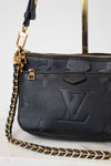 A close-up of a black Louis Vuitton shoulder bag with a pebbled leather texture, embossed monogram pattern, gold-tone hardware, and a black-and-gold chain strap on a light marble surface.