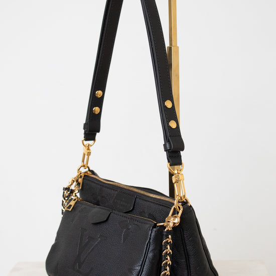 A black leather shoulder bag with gold-tone hardware, featuring a gold-tone metal  chain strap, shown on a white background.