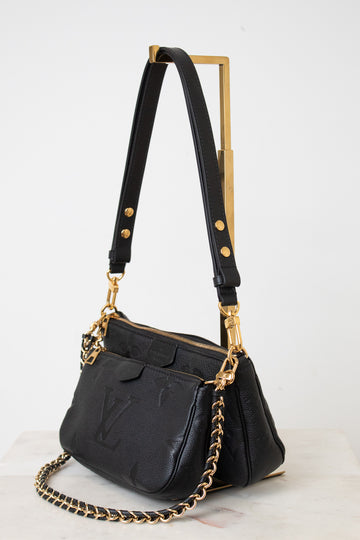 A black leather shoulder bag with gold-tone hardware, featuring a gold-tone metal  chain strap, shown on a white background.