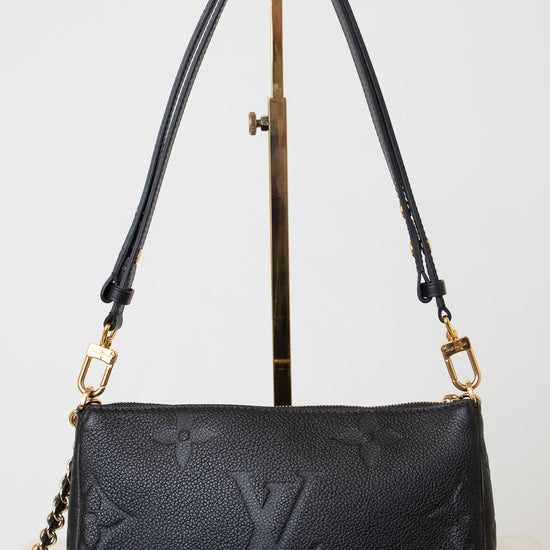 A black leather shoulder bag with gold-tone hardware and a chain strap, displayed on a  gold metal stand against a light gray background.