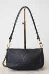 A black leather shoulder bag with gold-tone hardware and a chain strap, displayed on a  gold metal stand against a light gray background.