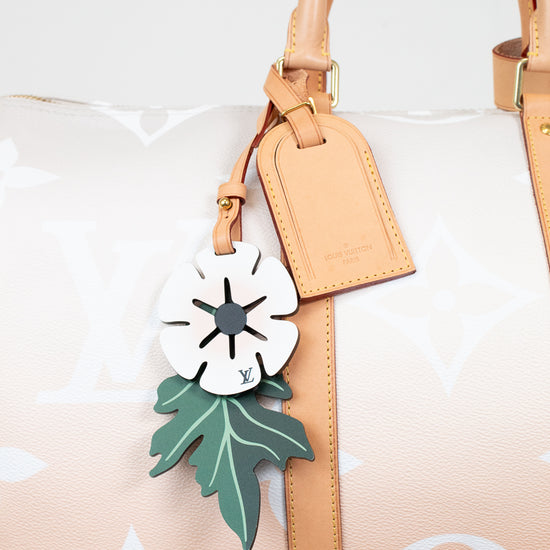 Handbag with a decorative tag featuring a white flower and green leaves on a light background